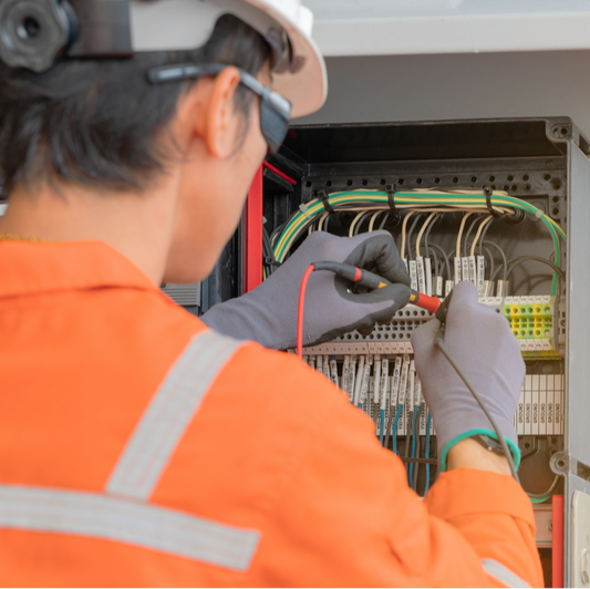 photo of man in orange safety work shirt doing electrical maintenance on a switchboard